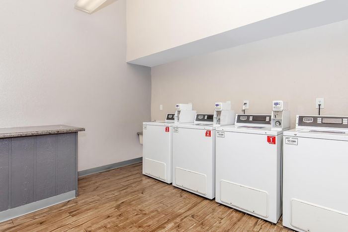 Modern laundry room with four sleek washers, bright setting, and wooden flooring for a clean and convenient apartment living experience.