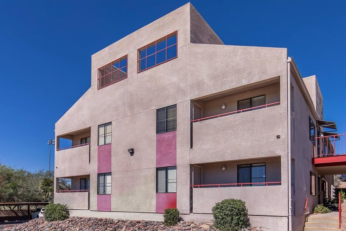 Contemporary apartment building with bold geometric design, featuring red accents and large windows under a clear blue sky.