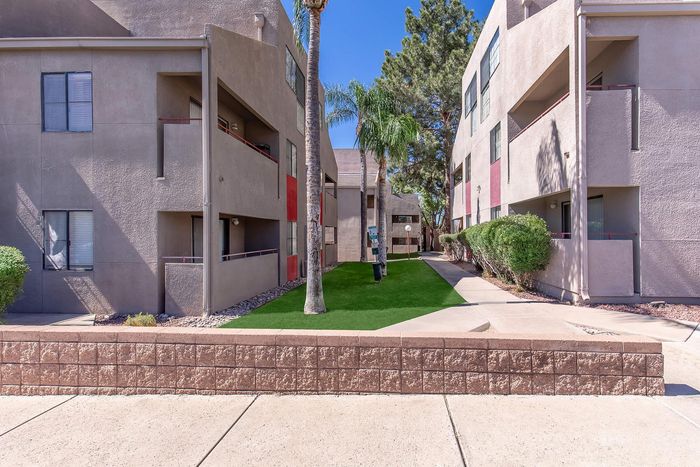Modern apartment complex with lush green landscaping, palm trees, and spacious outdoor walkways under a clear blue sky.