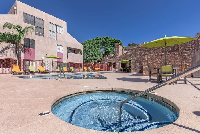 Luxurious apartment complex showcasing a sparkling whirlpool spa and inviting pool area with vibrant sun loungers and umbrellas, perfect for relaxation.
