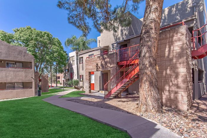 Charming apartment complex with modern architecture, vibrant red staircases, and lush green landscaping under a clear blue sky.