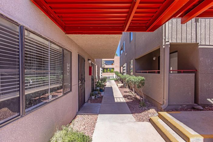 Inviting apartment walkway with vibrant red awning and lush greenery, offering a modern and welcoming entrance.