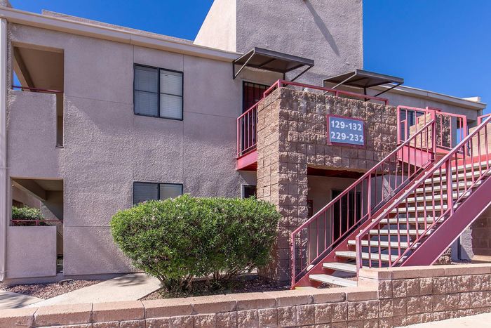 Charming apartment exterior with red railings and lush green bushes, featuring modern architecture and inviting entryway.