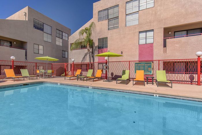 Inviting outdoor pool area with colorful lounge chairs and vibrant umbrellas, perfect for relaxation in a modern apartment complex.