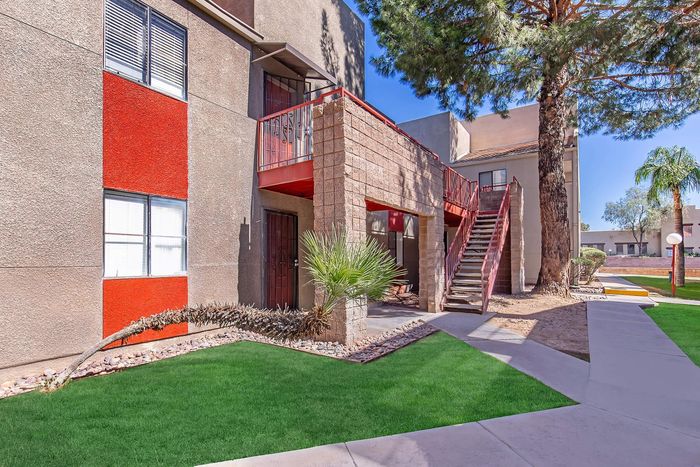 Charming apartment building with modern red accents, featuring lush green lawns and inviting outdoor walkways.