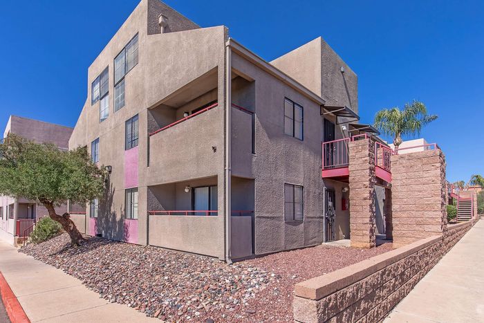 Modern apartment exterior featuring a unique geometric design, light-colored stucco finishes, and vibrant red accents, surrounded by a landscaped stone garden.