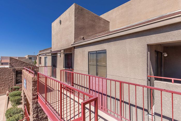 Charming apartment exterior with sleek red railings and modern architecture under a brilliant blue sky.