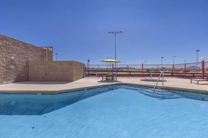 Inviting outdoor pool area with a sunny patio, umbrella-shaded table, and clear blue sky, perfect for relaxation.