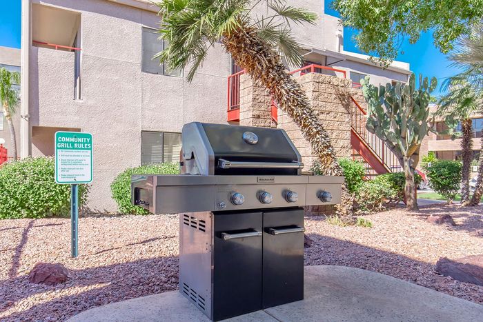 Inviting community BBQ area surrounded by lush greenery and modern apartment buildings under the bright blue sky.