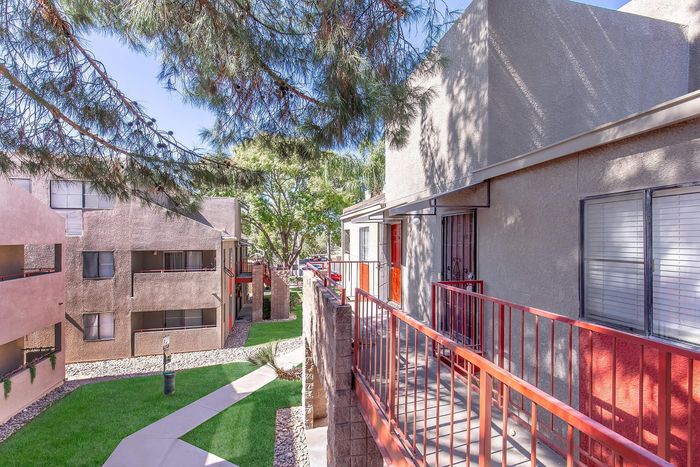 Charming apartment exterior showcasing a peaceful walkway, modern railings, and lush trees under a bright blue sky.