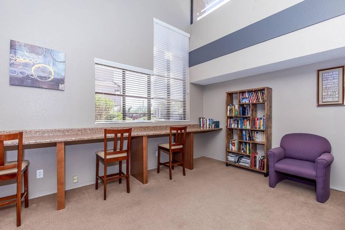 Bright communal study area with modern decor, featuring a long shared desk, comfortable seating, and a well-stocked bookshelf.