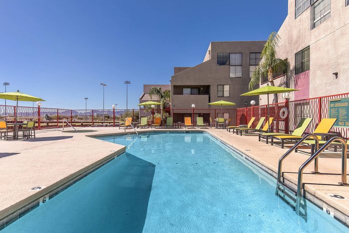 Inviting apartment complex pool area with modern lounge chairs, vibrant umbrellas, and scenic views under a clear blue sky.