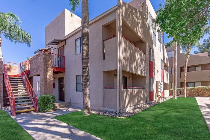 Charming apartment exterior featuring modern architecture, lush green landscaping, and inviting stairways under a clear blue sky.
