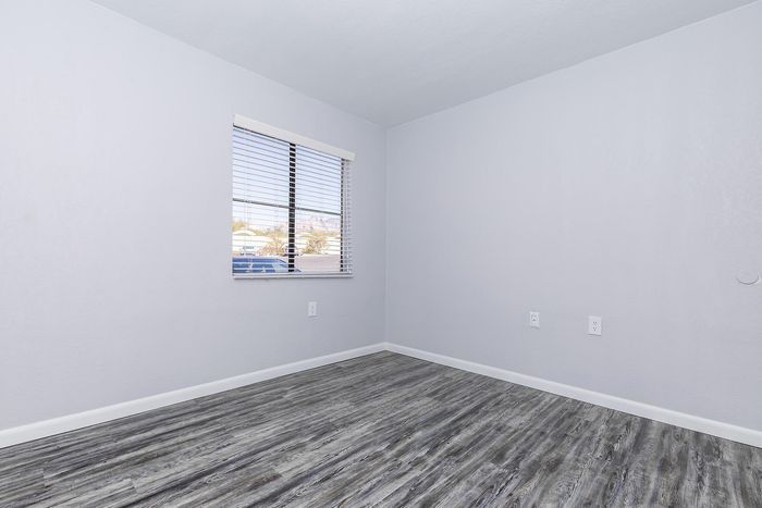 Bright, empty room with sleek gray laminate flooring and a large window offering natural light and a pleasant view.
