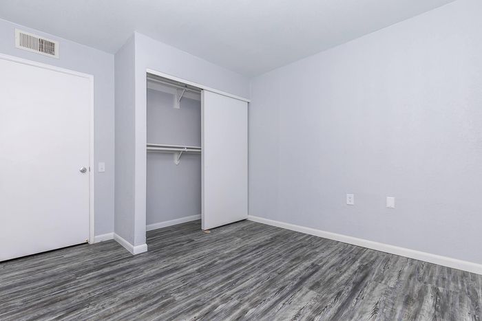 Inviting bedroom with clean white walls, spacious closet, and sleek gray laminate flooring, offering a modern and airy atmosphere.