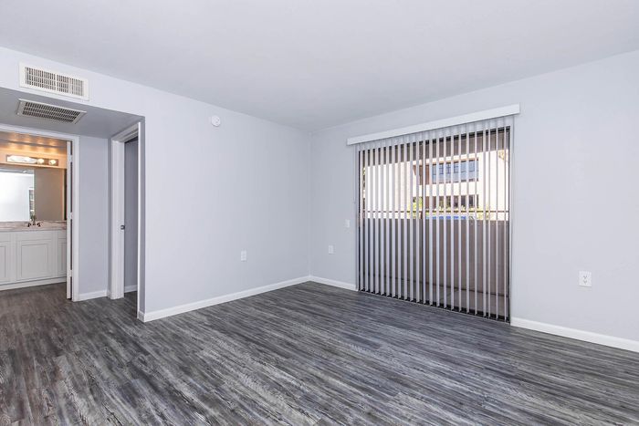 Bright and spacious room with elegant wood flooring, sliding glass doors leading to a balcony, and an inviting bathroom entrance.