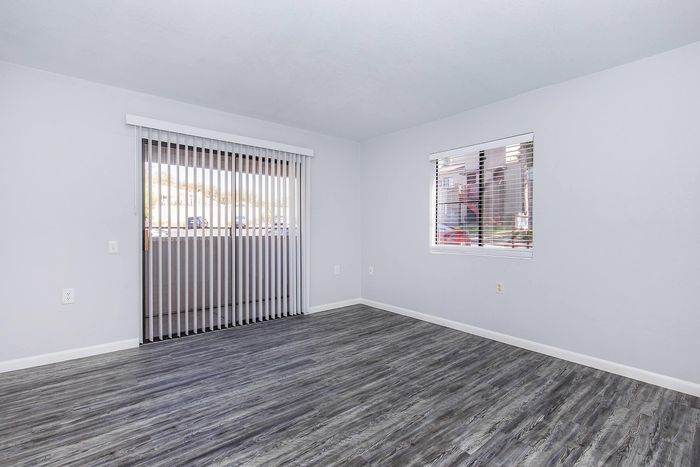 Bright and airy living space with sleek gray hardwood floors, vertical blinds, and large windows offering abundant natural light.