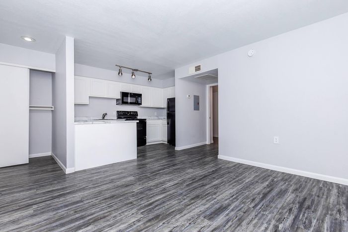 Modern apartment with sleek laminate flooring, open kitchen plan featuring white cabinetry, black appliances, and cozy lighting.