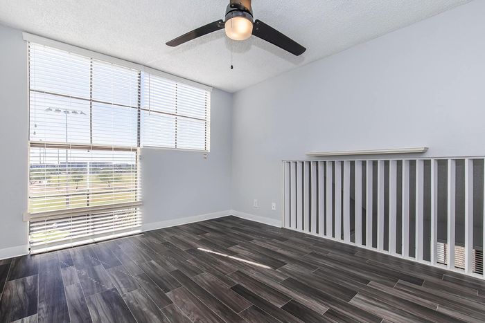 Bright and modern room with sleek wood flooring, large windows, and a stylish ceiling fan, offering a perfect blend of comfort and elegance.