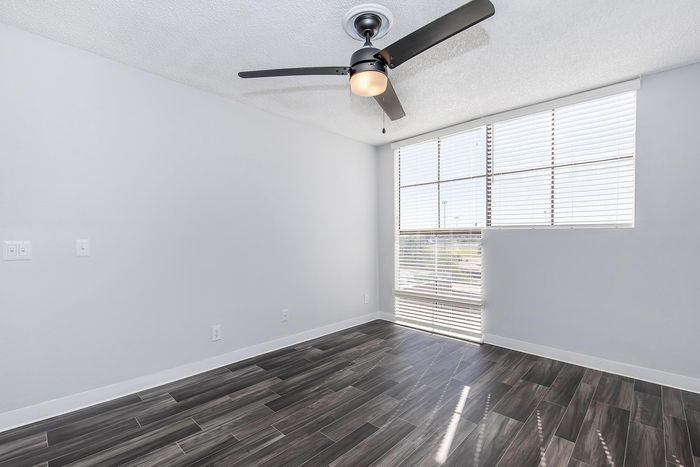 Bright and airy room with modern wood flooring, large window with blinds, and a sleek ceiling fan.