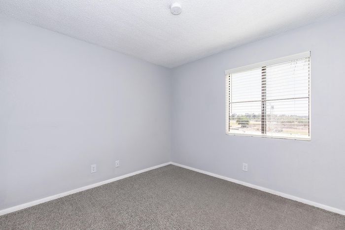 Bright and inviting bedroom with large window, plush carpeting, and modern neutral walls.