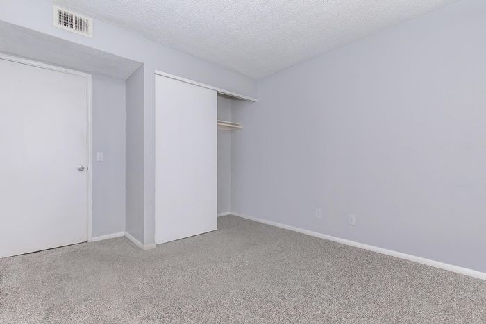 Spacious bedroom with fresh grey carpeting, ample natural light, and a convenient built-in closet.