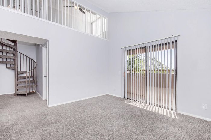 Bright modern living space with plush carpeting, spiral staircase, and sliding glass door opening to a balcony.