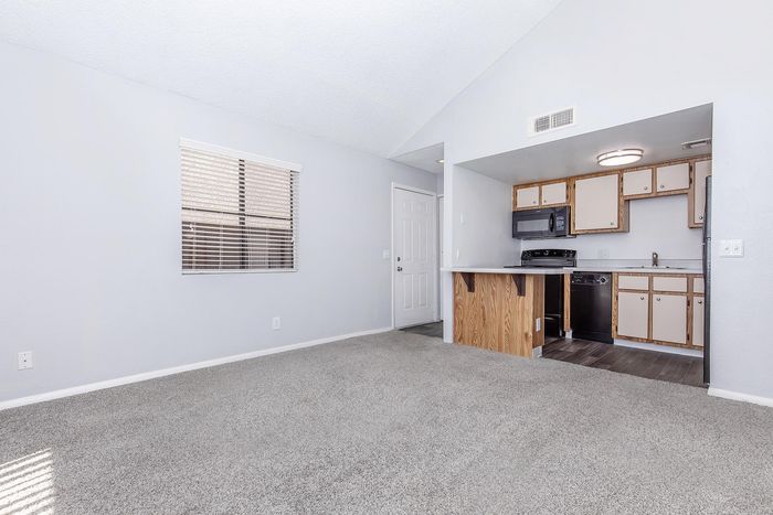 Bright and airy living area with plush carpet, adjacent to a cozy kitchen featuring wooden cabinetry and modern appliances.