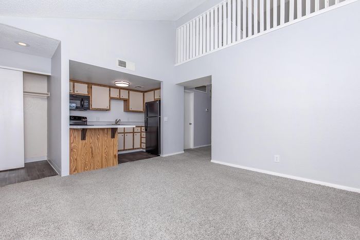 Bright apartment interior featuring a cozy carpeted living area, an open kitchen with wooden cabinets, and a stylish loft railing above.