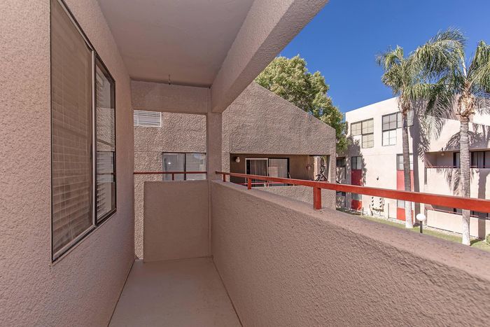 Charming apartment balcony with a modern railing overlooking a lush courtyard with palm trees and inviting sunlight.