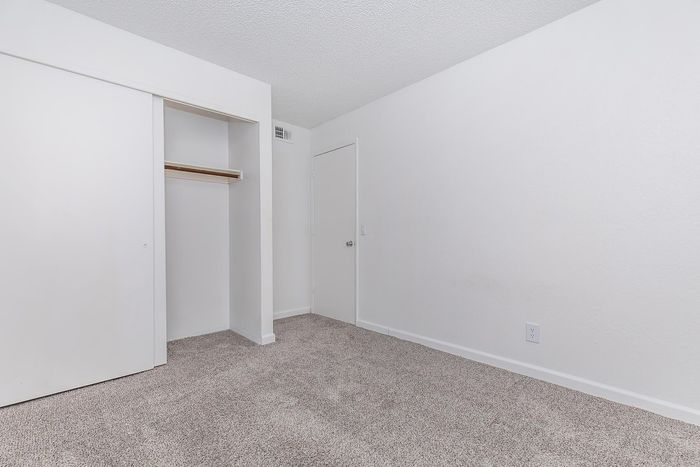 Bright and spacious bedroom with plush carpet flooring and ample closet space, perfect for comfortable living.