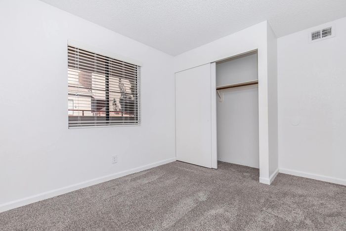 Bright bedroom with clean neutral carpet, large window with blinds, and spacious closet.