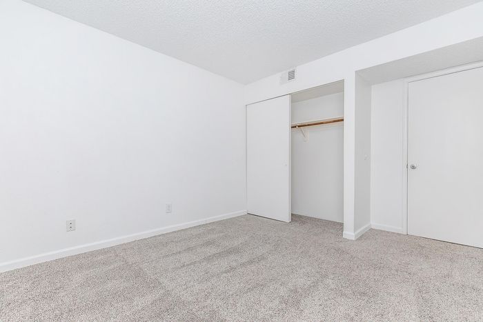 Pristine room with plush carpeting, fresh white walls, and a spacious closet, offering a blank canvas for personalized design.