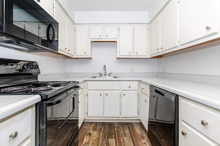 Stylish modern kitchen with sleek black appliances, white cabinetry, and elegant wood flooring.