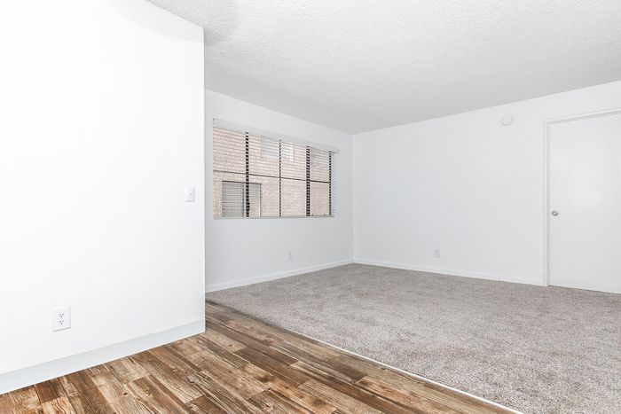 Bright and airy room with elegant wood flooring and plush carpet, featuring large windows for natural light.