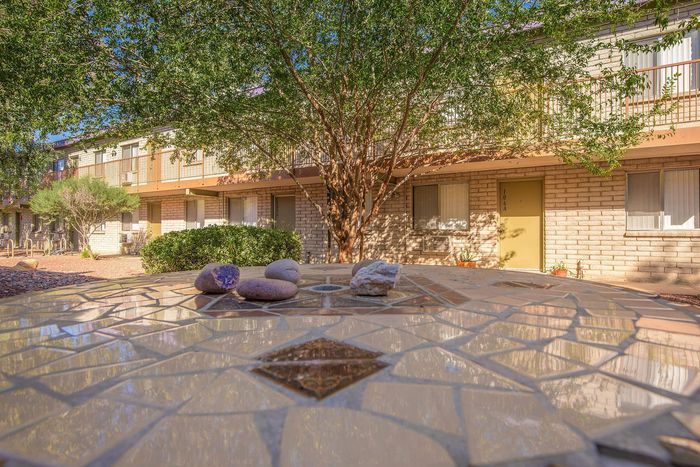 Charming apartment exterior with natural brick facade, nestled among lush greenery and a stylish mosaic table in the foreground.