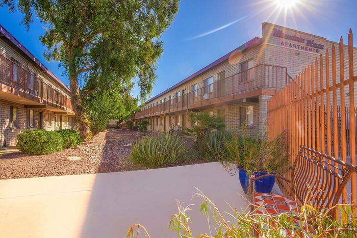 Inviting apartment complex featuring charming brick buildings, lush greenery, and warm sunlight filtering through, offering a serene living environment.