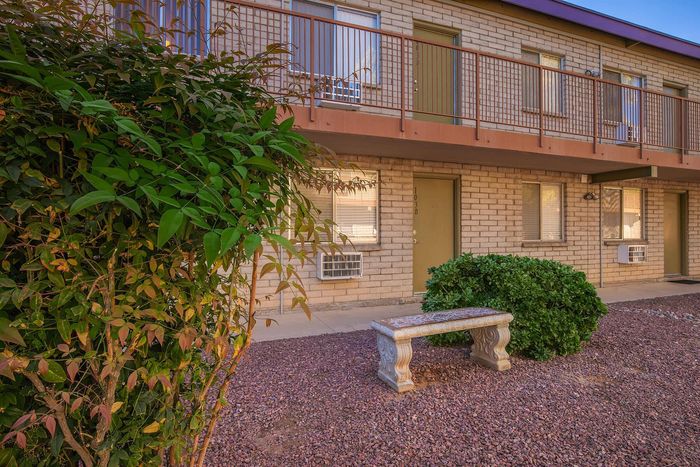 Inviting apartment exterior with charming brick facade, a lush green shrub, and a classic stone bench in a serene courtyard.