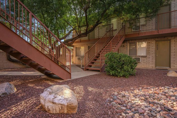 Charming apartment exterior with modern metal staircases, lush greenery, and inviting natural landscaping.