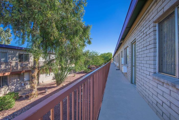 Charming apartment exterior with brick facade, lush greenery, and a sunny walkway.