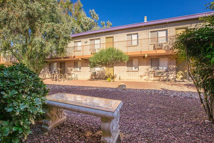 Charming apartment complex with lush greenery, stone pathways, and a decorative bench for relaxation.