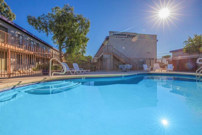 Inviting apartment complex with a sparkling pool surrounded by sunlit lounging areas and lush greenery, perfect for summer relaxation.