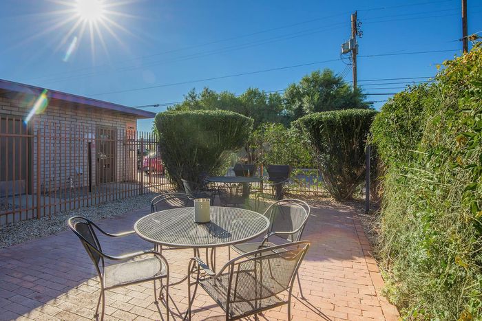 Charming outdoor patio with a sunlit ambiance, featuring a stylish metal table set, surrounded by lush greenery and privacy fence.