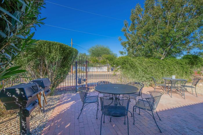 Charming outdoor patio with metal furniture, surrounded by lush greenery and a vibrant blue sky, perfect for leisure and barbecues.