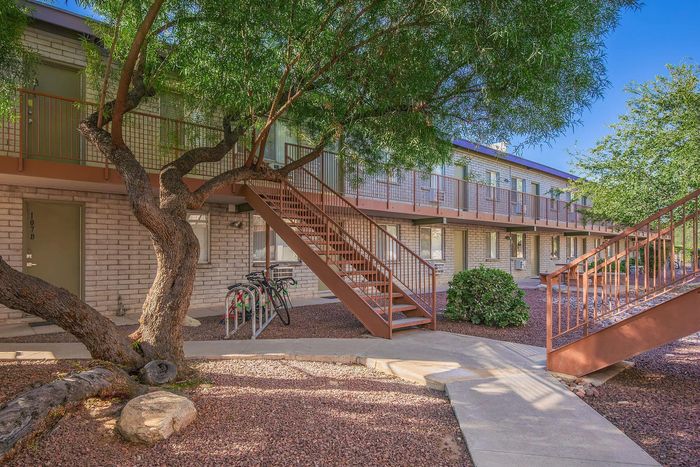 Charming apartment complex with upper-level walkway, nestled among lush trees and inviting landscaping.