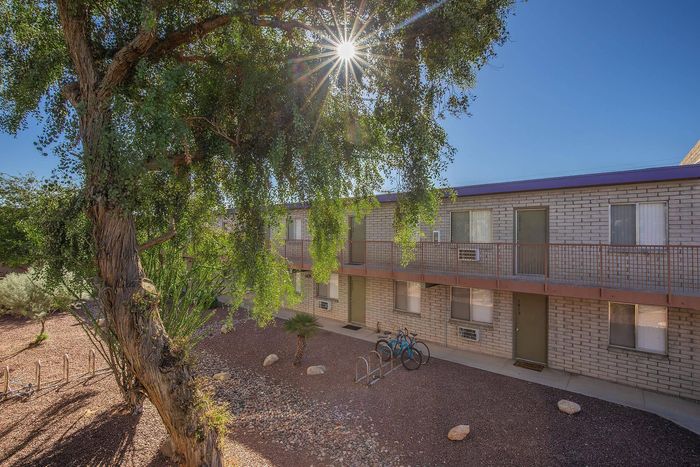 Charming apartment exterior with sunlit brick facade, lush greenery, and convenient bicycle racks.