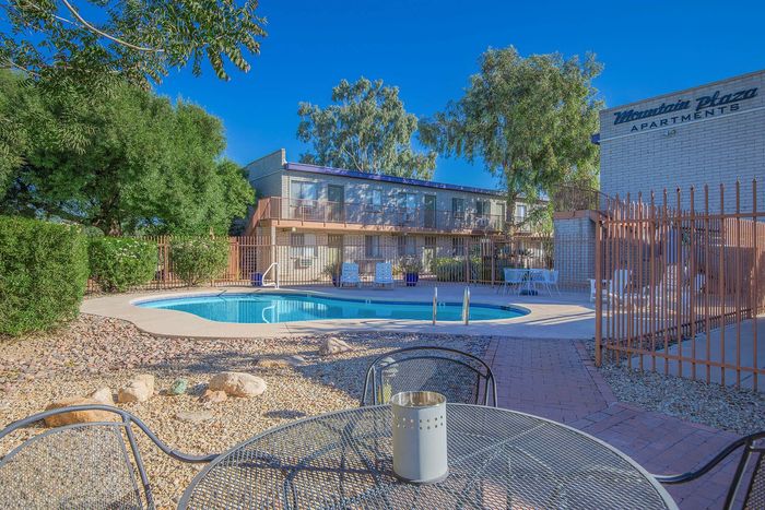 Sunny apartment complex featuring a sparkling pool, lush greenery, and inviting outdoor seating&mdash;perfect for relaxation and gatherings.