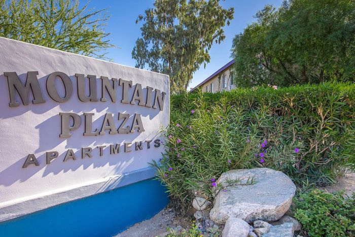 Inviting entrance to Mountain Plaza Apartments, surrounded by lush greenery and vibrant flowers.