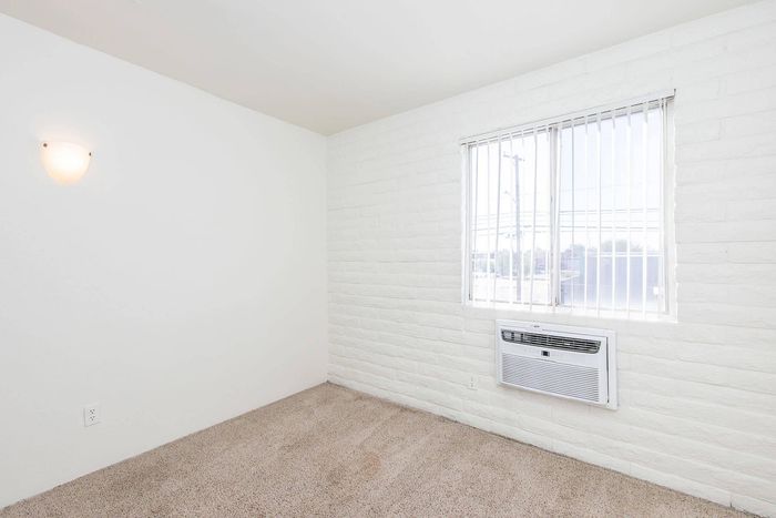 Bright and airy room with plush carpet, a large window, and a modern wall-mounted air conditioner.