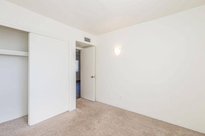 Bright, airy bedroom with fresh white walls, modern light fixture, and plush carpet, complemented by a spacious closet with sliding doors.